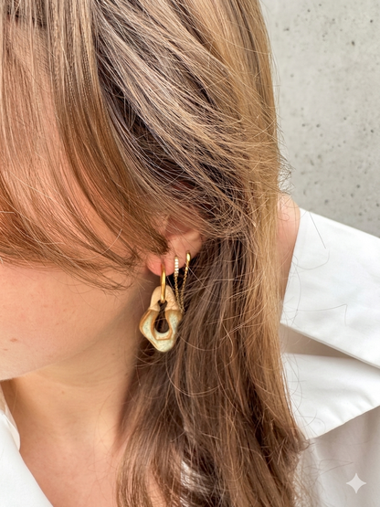Handmade ceramic hoop earrings in grey green glaze worn by a model against a whitewashed Portuguese wall in warm golden light — Mosca collection by Jadeo Studio Lisbon