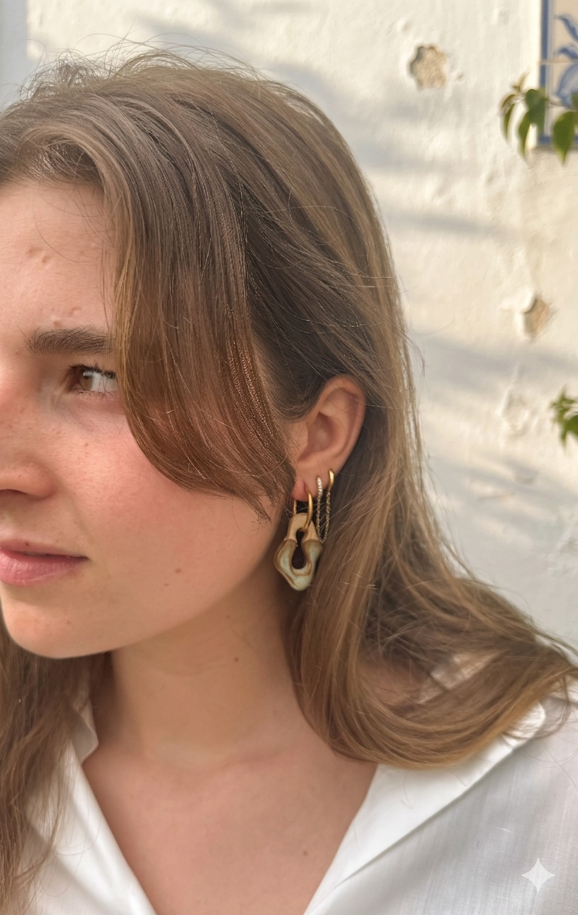 Side profile of model wearing grey green handmade ceramic earrings with gold hoops and chain, white brick wall background — Mosca collection by Jadeo Studio Lisbon