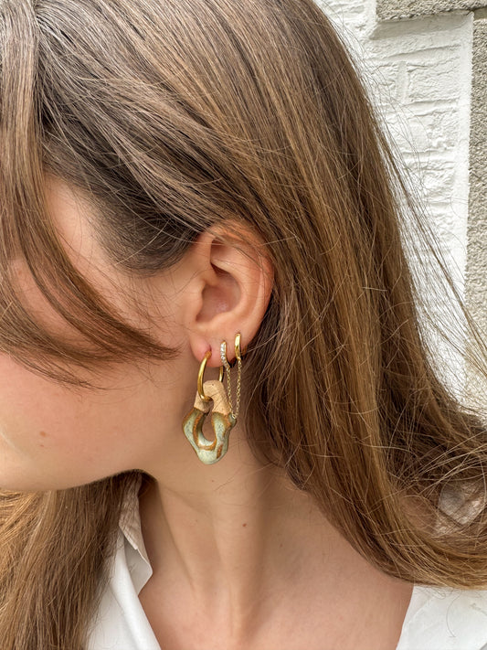 Close-up of grey green ceramic earrings with gold hoop and chain detail on a model, soft concrete studio background — Mosca handmade ceramic jewelry by Jadeo Studio Lisbon