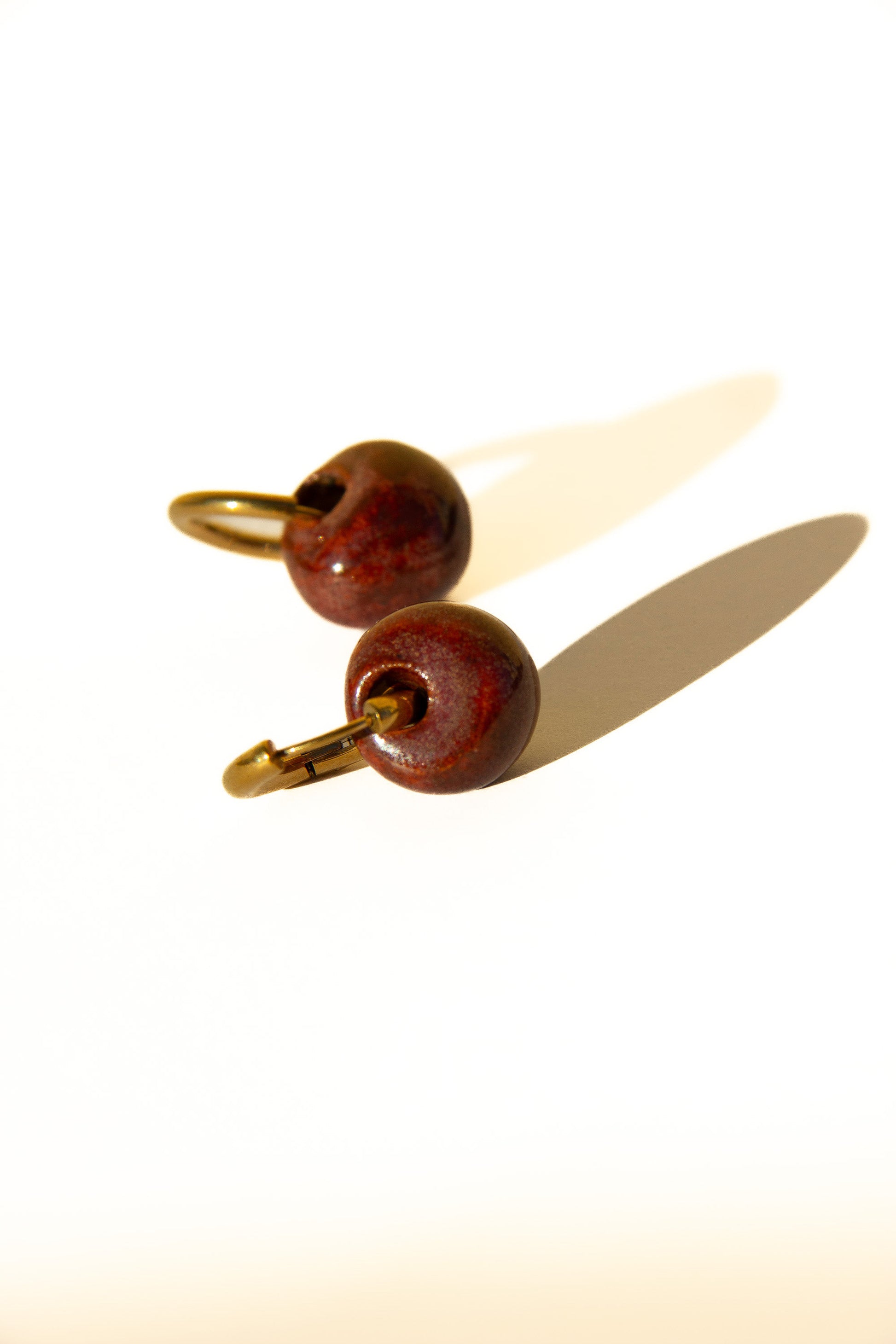 Gomes handmade ceramic earrings in Burgundy — rounded circular form, bold yet discreet, deep wine red glaze, made in Lisbon Portugal by Jadeo Studio