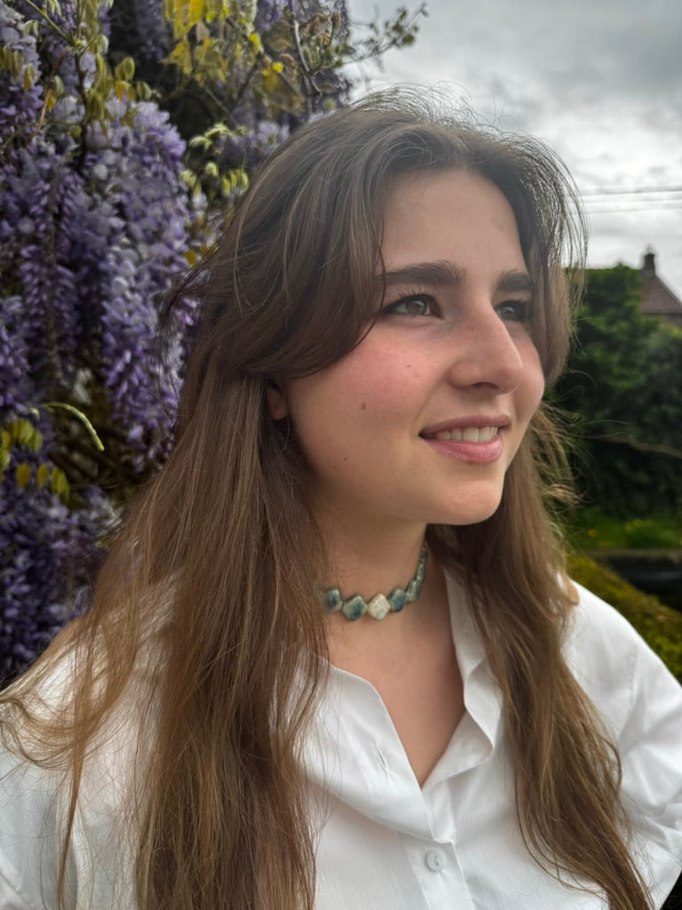 Monti handmade ceramic choker necklace in Sparkling Blue and White — sculptural beads inspired by Roman architecture, made in Lisbon Portugal by Jadeo Studio, with flower background