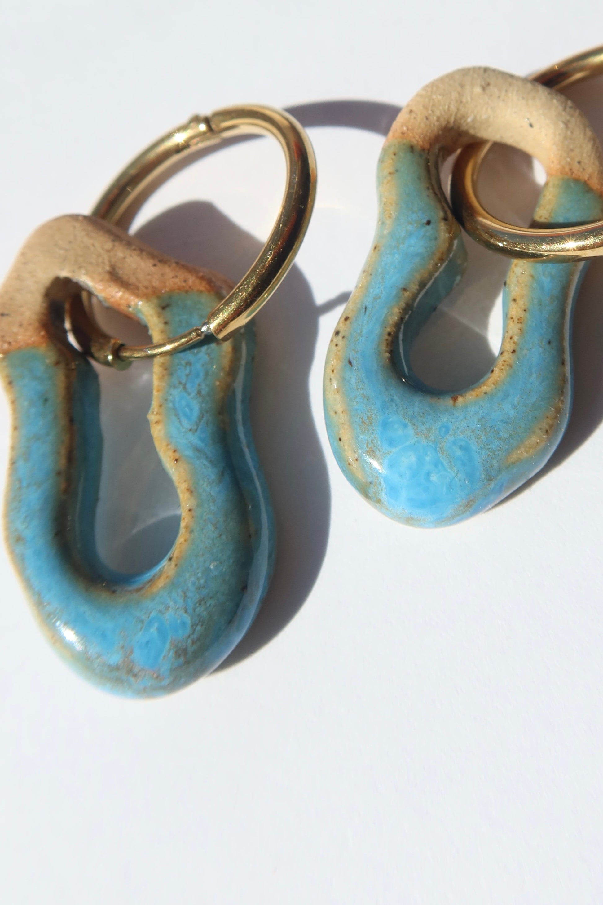 Mosca handmade ceramic earrings in Blue Sky — organic sculpted clay with glossy glaze, pair displayed in natural sunlight with soft shadow, made in Lisbon Portugal by Jadeo Studio