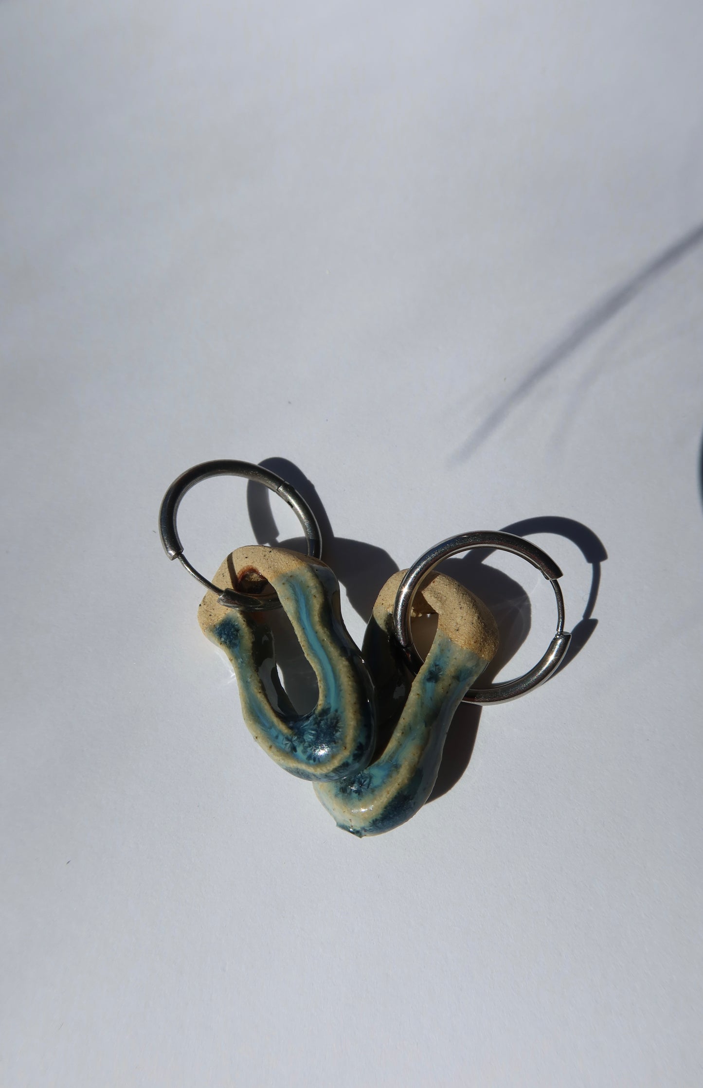 Mosca sparkling blue ceramic earrings — sculptural handmade clay with glossy finish, artistic composition in natural sunlight, crafted in Lisbon Portugal by Jadeo Studio