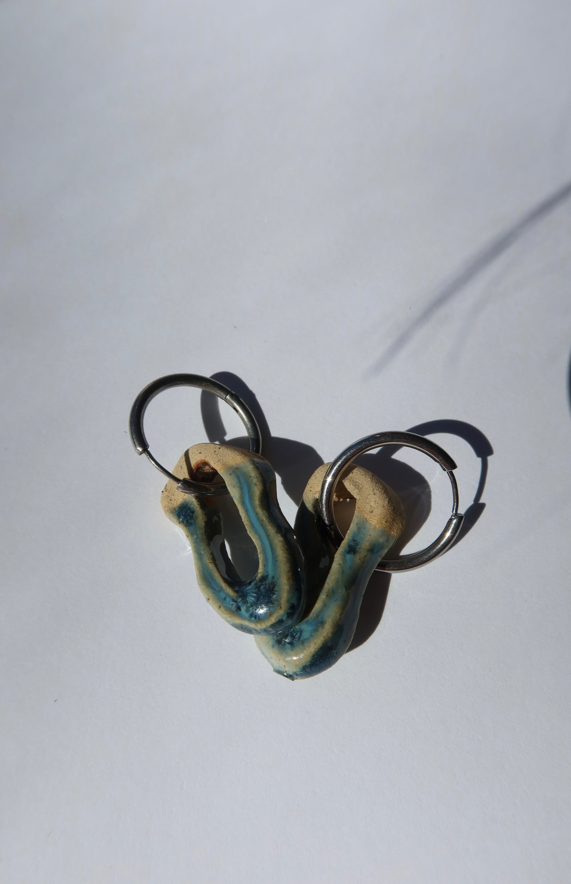 Mosca sparkling blue ceramic earrings — sculptural handmade clay with glossy finish, artistic composition in natural sunlight, crafted in Lisbon Portugal by Jadeo Studio