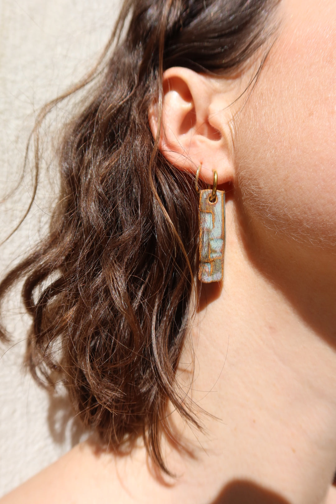 Penha handmade ceramic earrings in Grey Green on curly hair model — minimalist rectangular drop, sculpted clay, made in Lisbon Portugal by Jadeo Studio